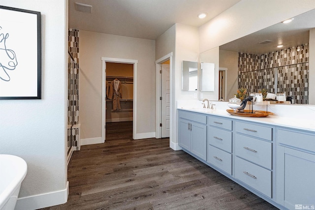 full bath featuring a sink, double vanity, baseboards, wood finished floors, and a soaking tub
