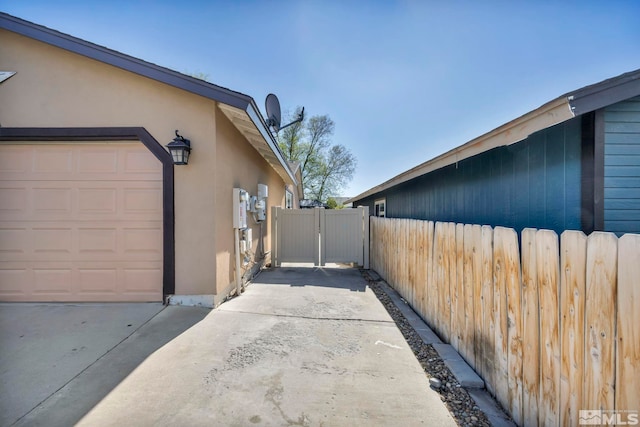 view of side of home featuring fence, a gate, stucco siding, and driveway