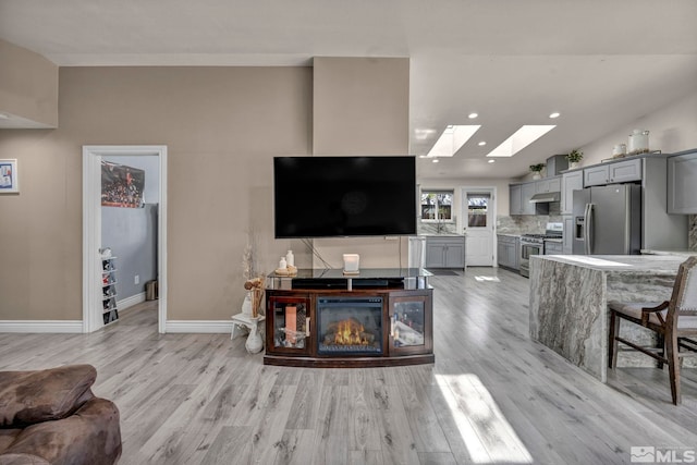 living area with a skylight, baseboards, recessed lighting, and light wood-style flooring