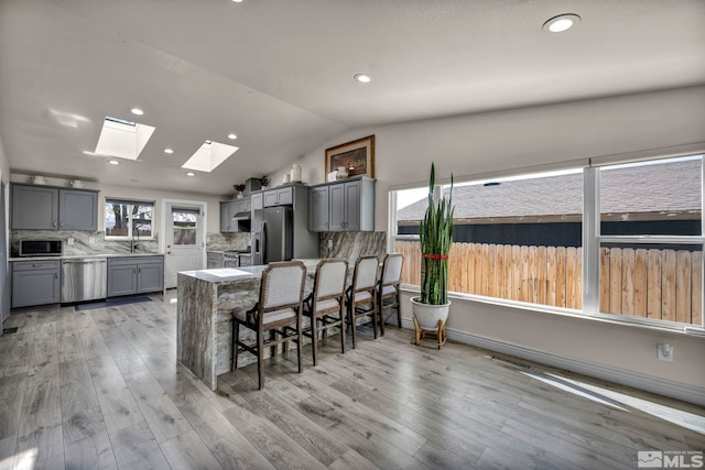 kitchen featuring vaulted ceiling with skylight, gray cabinets, stainless steel appliances, and light wood-type flooring