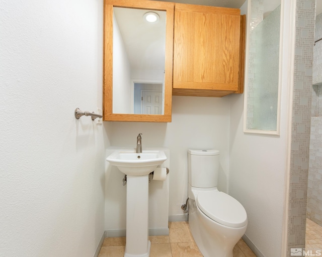 bathroom featuring toilet, tile patterned floors, a tile shower, and baseboards