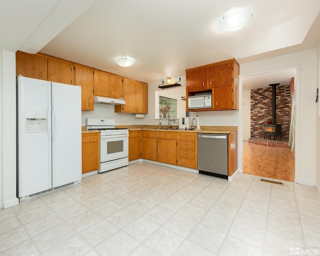 kitchen featuring light countertops, light floors, under cabinet range hood, and white appliances