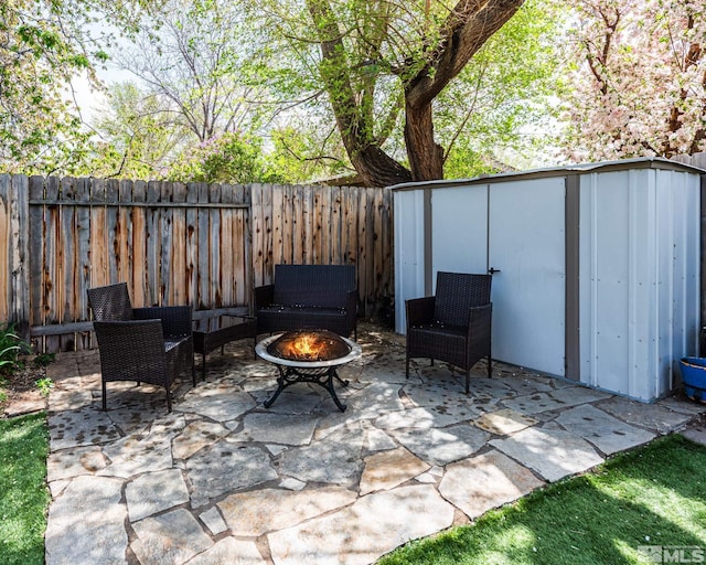 view of patio / terrace with a fenced backyard, a storage unit, an outbuilding, and a fire pit
