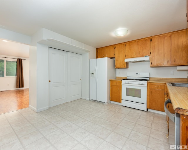 kitchen featuring light countertops, a sink, light floors, under cabinet range hood, and white appliances