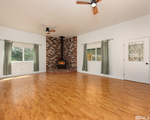 unfurnished living room with light wood-style floors, a wood stove, and ceiling fan