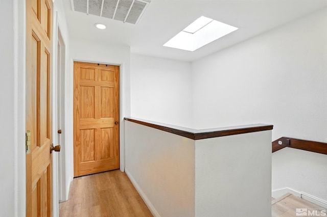 hall featuring a skylight, baseboards, light wood-style flooring, and visible vents