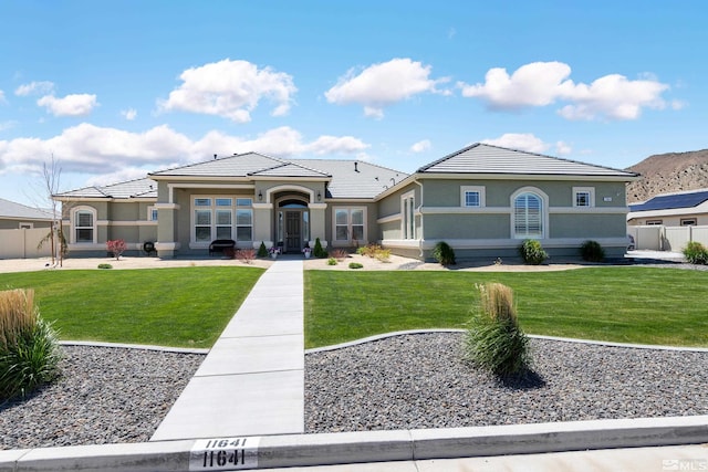 view of front of house with fence, stucco siding, a tiled roof, and a front lawn