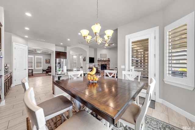 dining area featuring a fireplace, arched walkways, ceiling fan with notable chandelier, recessed lighting, and baseboards
