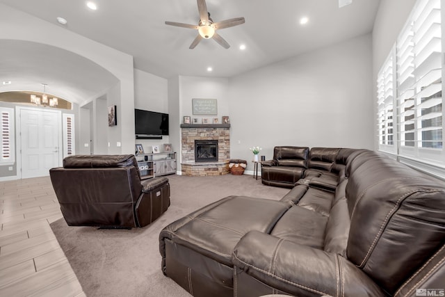 living room featuring lofted ceiling, a stone fireplace, recessed lighting, light wood-type flooring, and ceiling fan with notable chandelier