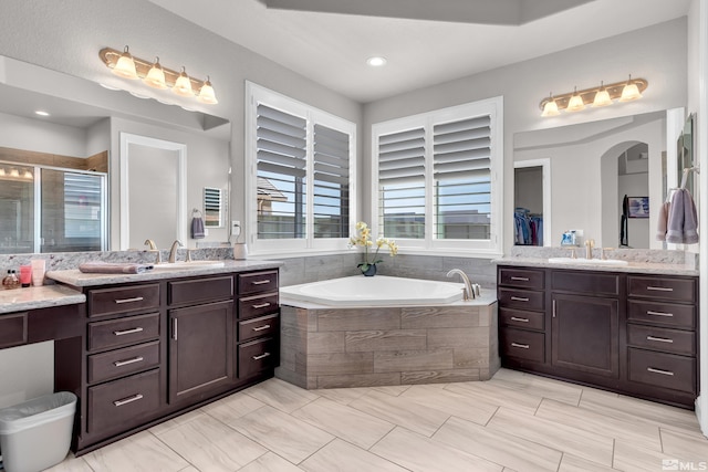 bathroom featuring a sink, a stall shower, a bath, and two vanities