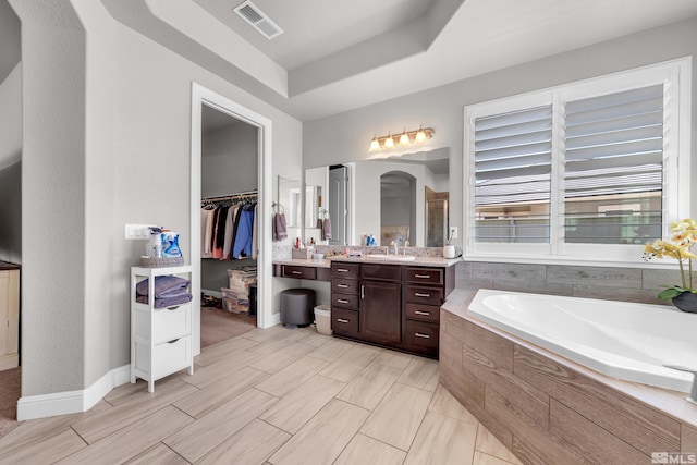 full bath with a walk in closet, a raised ceiling, vanity, visible vents, and a garden tub