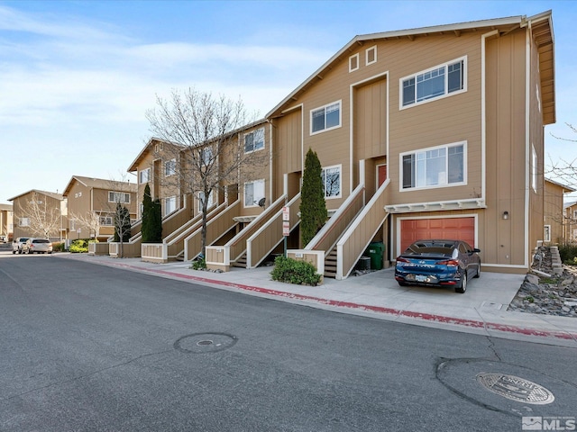 view of building exterior featuring stairs, an attached garage, driveway, and a residential view