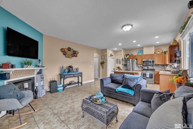 living room featuring a glass covered fireplace, light tile patterned flooring, baseboards, recessed lighting, and arched walkways