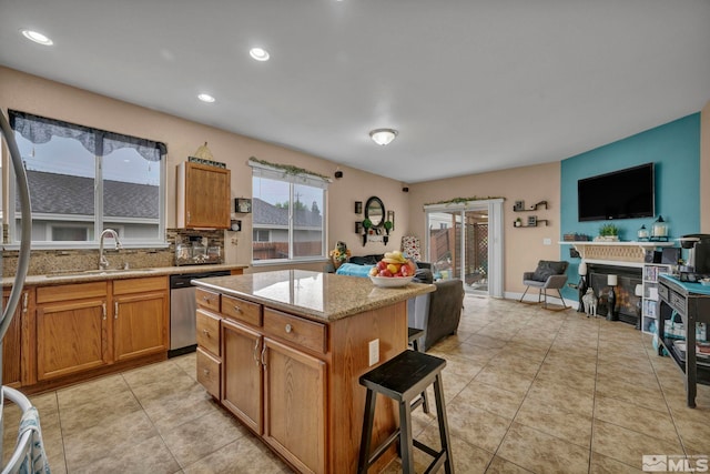 kitchen featuring a breakfast bar area, dishwasher, a sink, light stone counters, and open floor plan