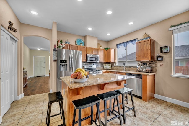 kitchen featuring light stone countertops, a sink, arched walkways, stainless steel appliances, and decorative backsplash