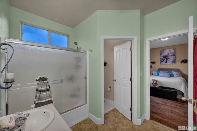 ensuite bathroom with a sink, tile patterned floors, baseboards, combined bath / shower with glass door, and ensuite bathroom