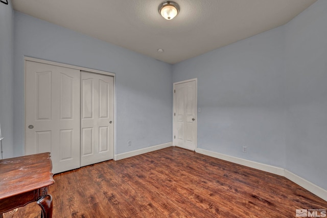 unfurnished bedroom featuring baseboards, dark wood-style flooring, and a closet