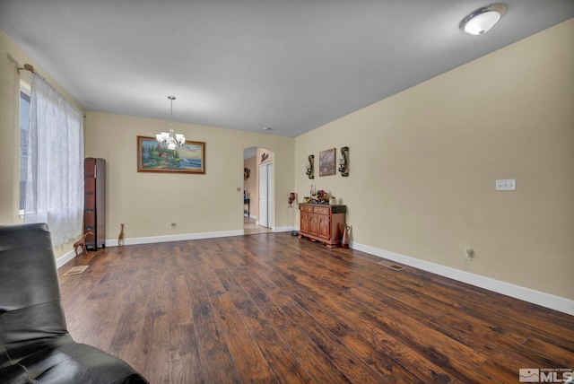 unfurnished living room with arched walkways, baseboards, dark wood finished floors, and an inviting chandelier