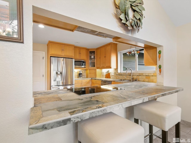 kitchen with a peninsula, glass insert cabinets, tasteful backsplash, a sink, and appliances with stainless steel finishes