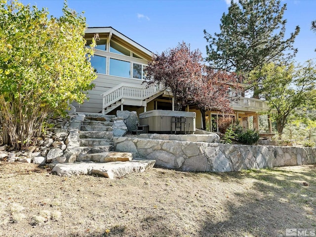 rear view of house with a hot tub, a wooden deck, and stairs