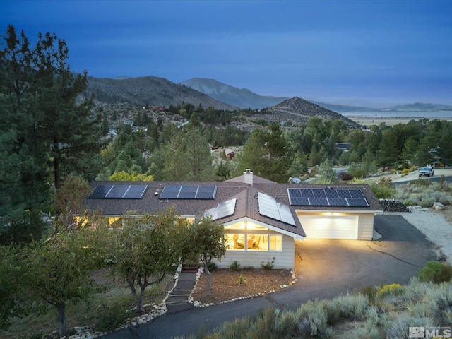 view of front of home featuring a shingled roof, a garage, dirt driveway, a mountain view, and solar panels
