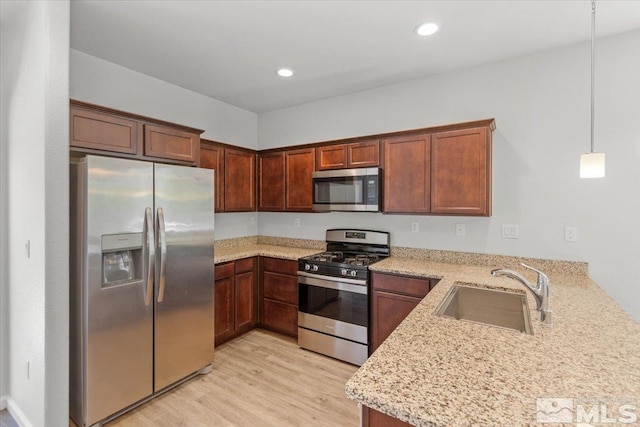 kitchen with appliances with stainless steel finishes, light stone counters, a sink, light wood finished floors, and a peninsula