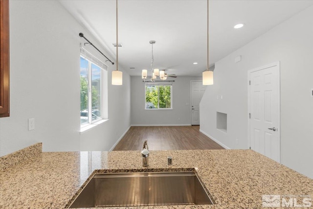 kitchen with light stone counters, an inviting chandelier, a sink, decorative light fixtures, and wood finished floors