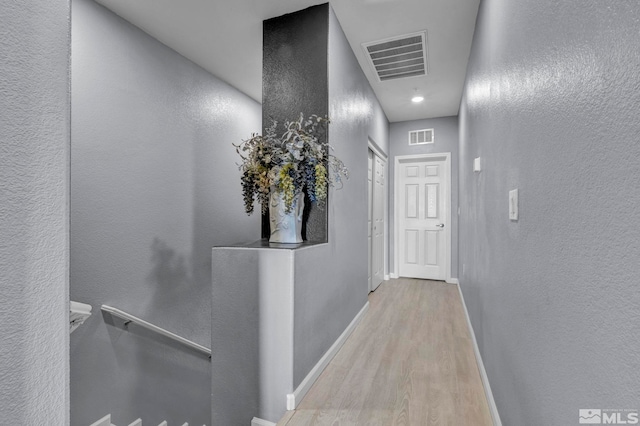 hallway featuring a textured wall, baseboards, an upstairs landing, wood finished floors, and visible vents
