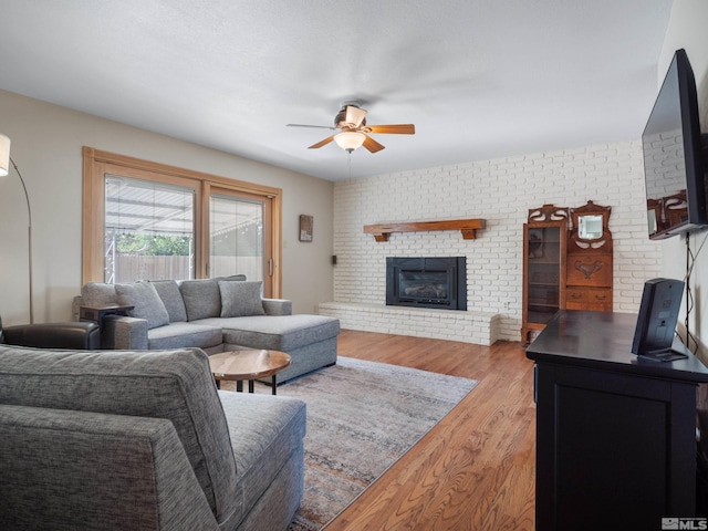 living room featuring a brick fireplace, ceiling fan, and wood finished floors