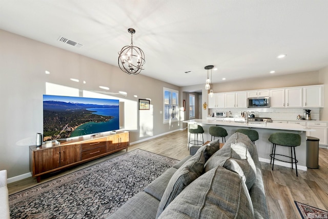 living area featuring an inviting chandelier, baseboards, light wood-type flooring, and visible vents