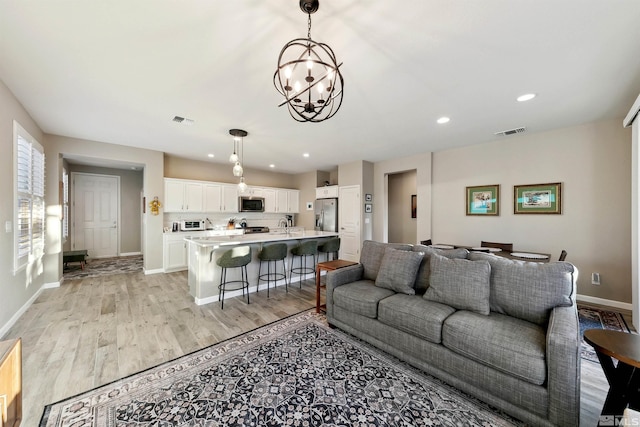 living room with a chandelier, baseboards, visible vents, and light wood-style floors