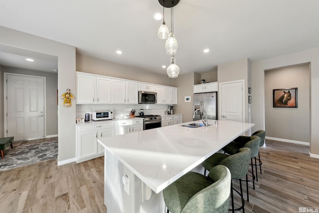 kitchen with a sink, baseboards, stainless steel appliances, and light wood-type flooring