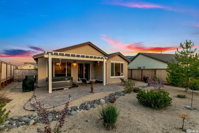 rear view of house with a fenced backyard, a hot tub, a patio area, and stucco siding