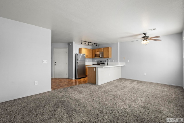 kitchen with a peninsula, dark carpet, ceiling fan, light countertops, and stainless steel appliances