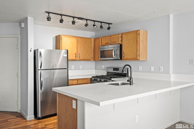 kitchen featuring a peninsula, wood finished floors, light countertops, a sink, and appliances with stainless steel finishes