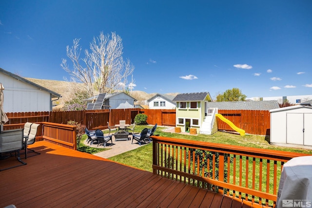 wooden terrace with an outdoor structure, a fenced backyard, a fire pit, and a storage shed