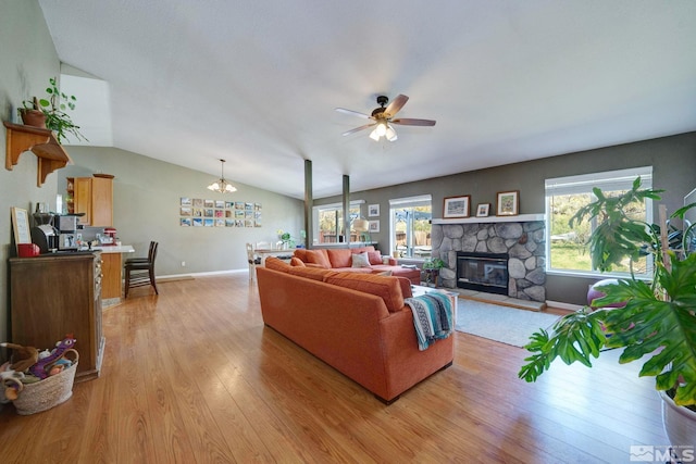 living area with a healthy amount of sunlight, a stone fireplace, ceiling fan with notable chandelier, and light wood-style flooring