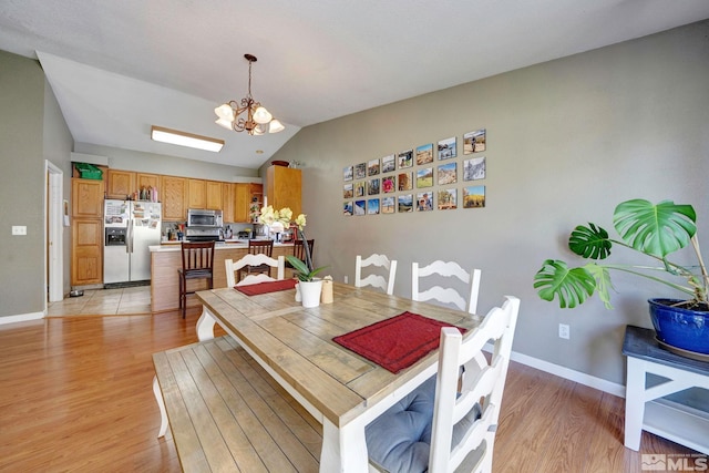 dining space with an inviting chandelier, baseboards, light wood-style flooring, and lofted ceiling