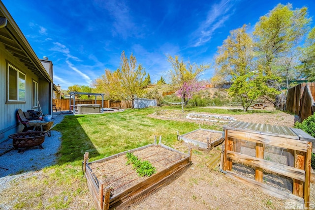 view of yard with a hot tub, a garden, a fenced backyard, and an outdoor fire pit