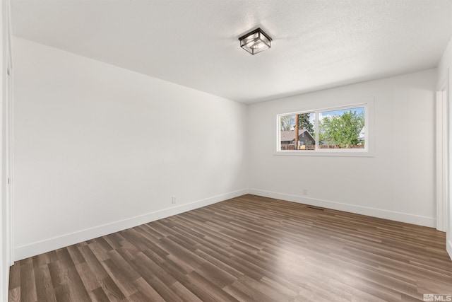 empty room featuring baseboards, a textured ceiling, and dark wood-style floors