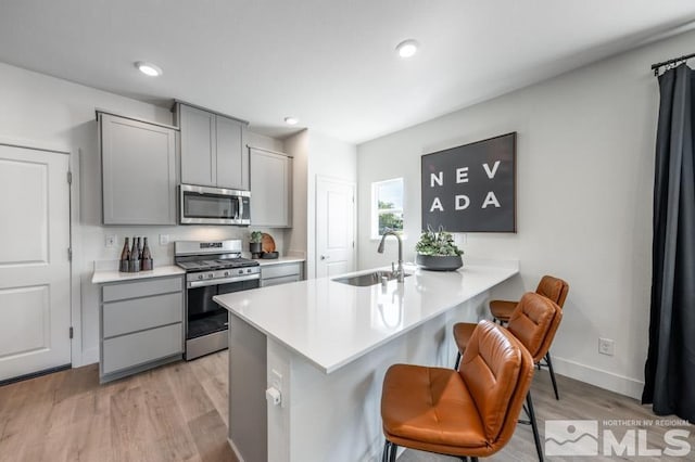kitchen featuring gray cabinetry, appliances with stainless steel finishes, a sink, and light wood-style floors