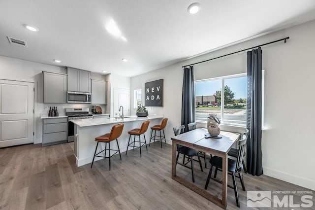 kitchen with visible vents, a breakfast bar, a sink, gray cabinetry, and stainless steel appliances