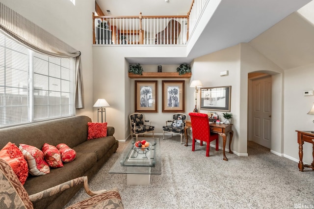 living area with carpet flooring, arched walkways, baseboards, and a towering ceiling