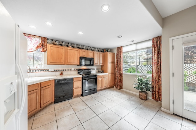 kitchen featuring a sink, black appliances, tile countertops, and a wealth of natural light