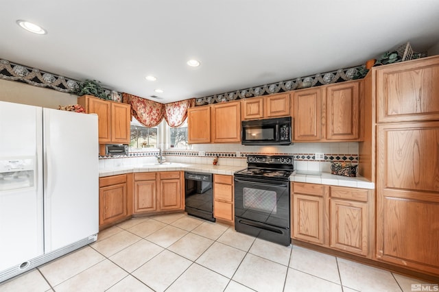 kitchen with light tile patterned flooring, a sink, tile countertops, tasteful backsplash, and black appliances