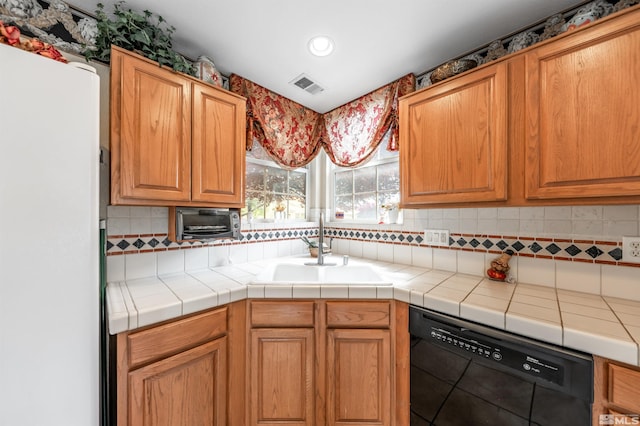 kitchen featuring visible vents, tasteful backsplash, dishwasher, a sink, and freestanding refrigerator