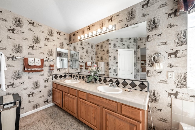 full bath featuring a sink, baseboards, tasteful backsplash, and wallpapered walls