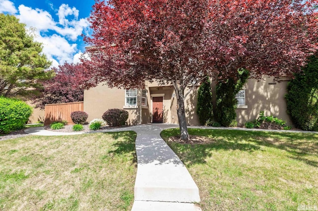 view of property hidden behind natural elements with fence, a front yard, and stucco siding