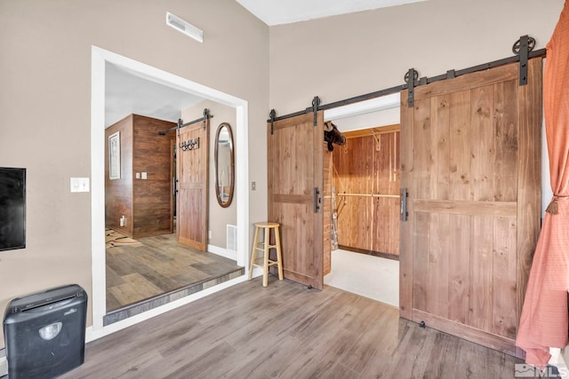 interior space with visible vents, a barn door, baseboards, and wood finished floors