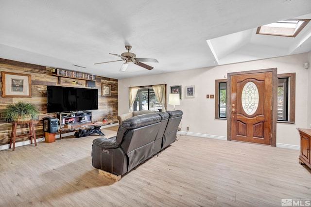 living room featuring a skylight, baseboards, a ceiling fan, and light wood-style flooring